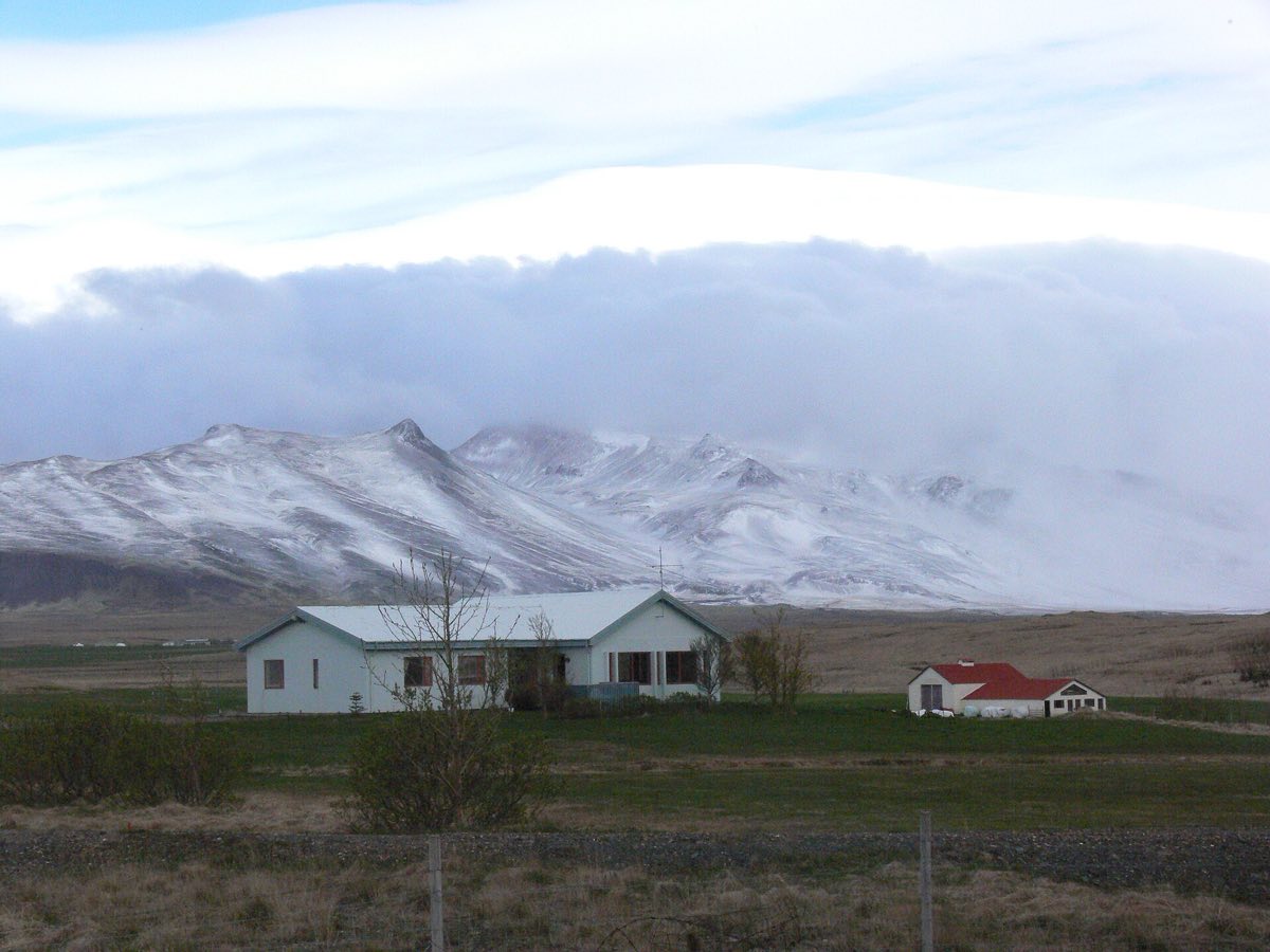 Bóndabær undir snævi þöktu fjalli.